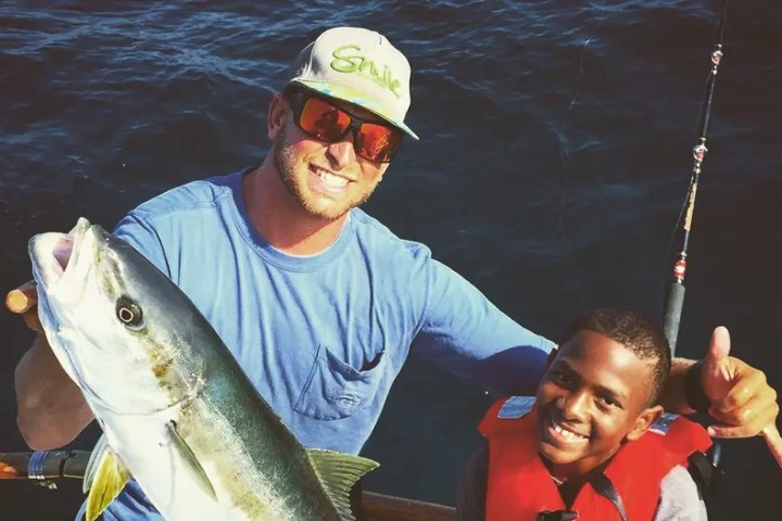 Two people on a boat, one holding a large fish, both smiling.