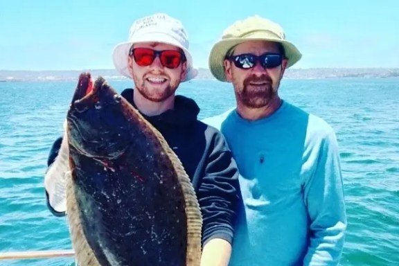 Two people on a boat holding a large fish with the ocean in the background.