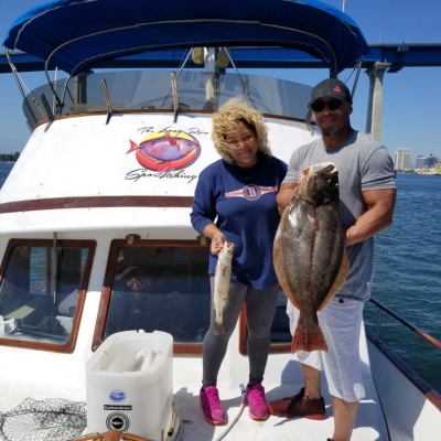 Two people on a boat holding fish, with a bridge in the background.