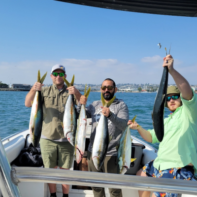 Three men on a boat hold freshly caught fish under a clear blue sky.