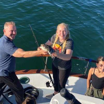 Three people on a boat holding a fish, with ocean in the background.