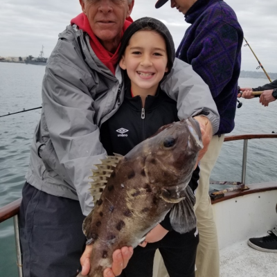 Two people holding a fish on a boat with water in the background.