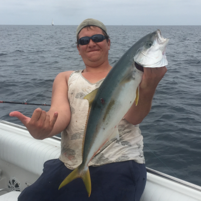 Person on a boat holding a large fish, smiling at the camera.