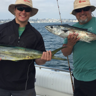 Two people on a boat holding large fish, with a city skyline in the background.