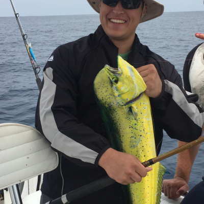 Person in a hat holding a yellow fish on a boat with fishing gear visible.