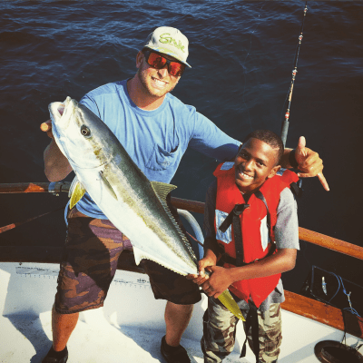 Two people on a boat, holding a large fish and smiling, one wearing a red life vest.