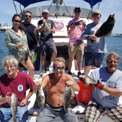 Group of people on a boat holding fish they caught, with a blue canopy above them.
