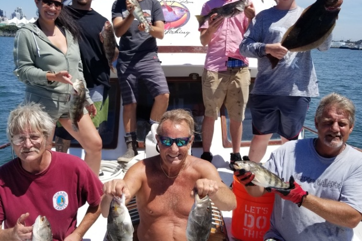 Group of people on a boat holding fish they caught, with a blue canopy above them.