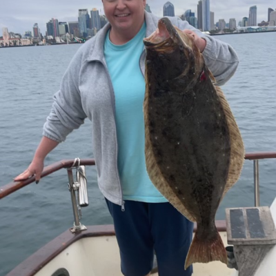 Person on a boat holding a large fish with a city skyline in the background.