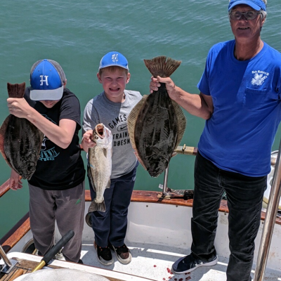 Three people on a boat holding up large fish in front of the ocean.
