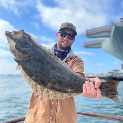 Man holding large fish on a boat with water and cloudy sky in background.