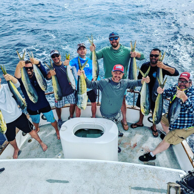 Eight men on a boat holding freshly caught fish over the ocean.