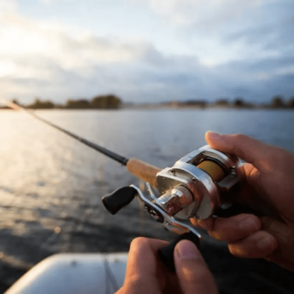 Person holding a fishing rod and reel over a calm lake at sunset.