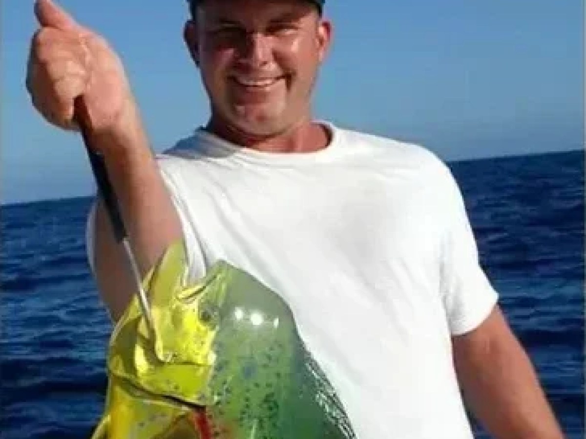 Man holding a large fish and a child holding a smaller fish, both smiling outdoors.